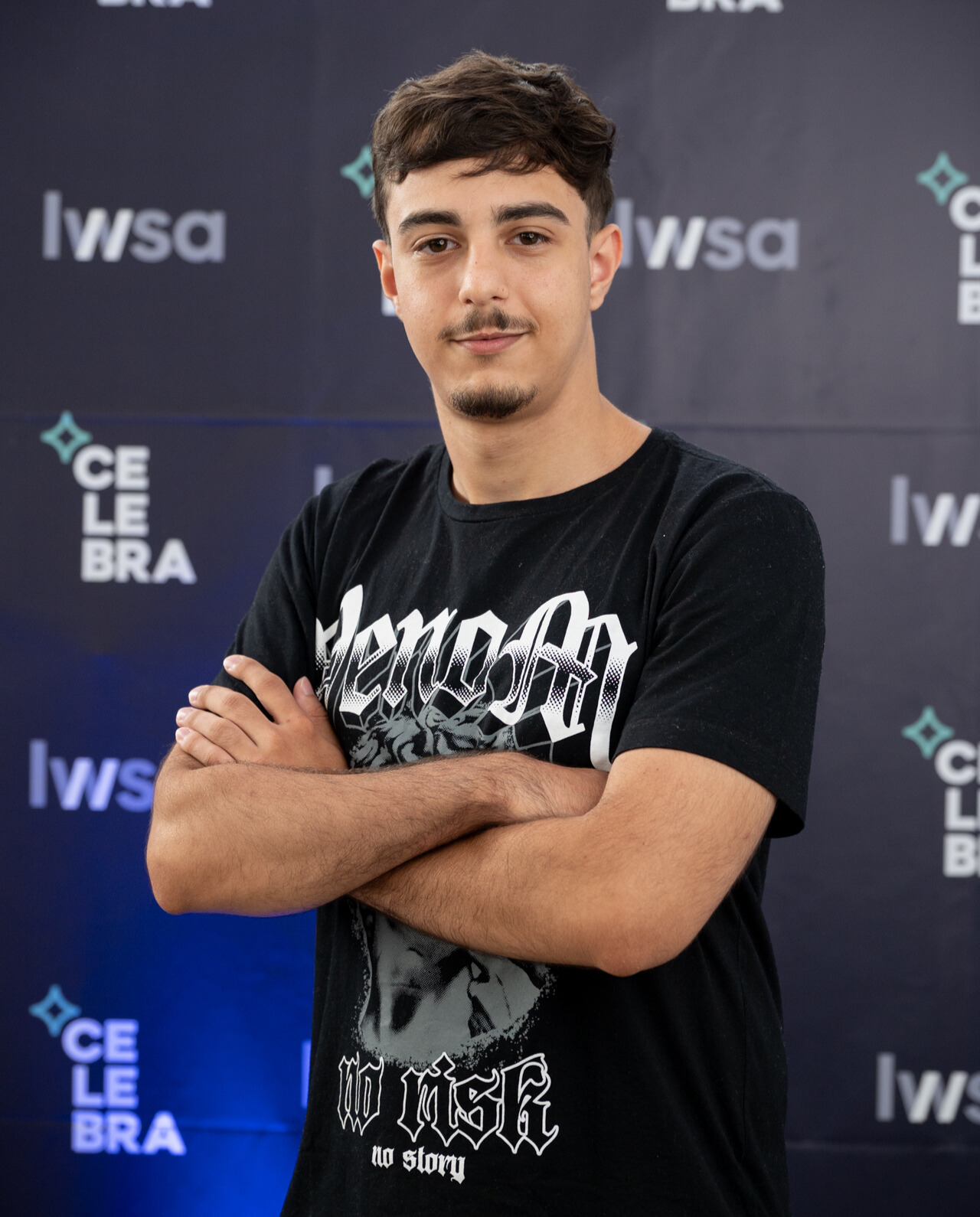 garoto de braço cruzado, camiseta preta e sorrindo